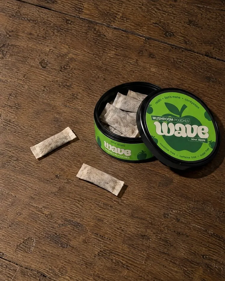 An open WAVE can with pouches inside and two loose pouches beside it.