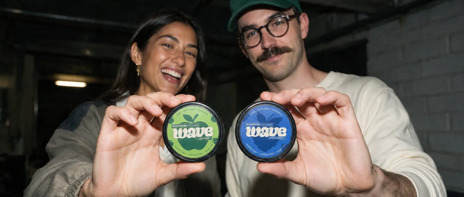 Two people holding WAVE cans — sour apple and blue raspberry.